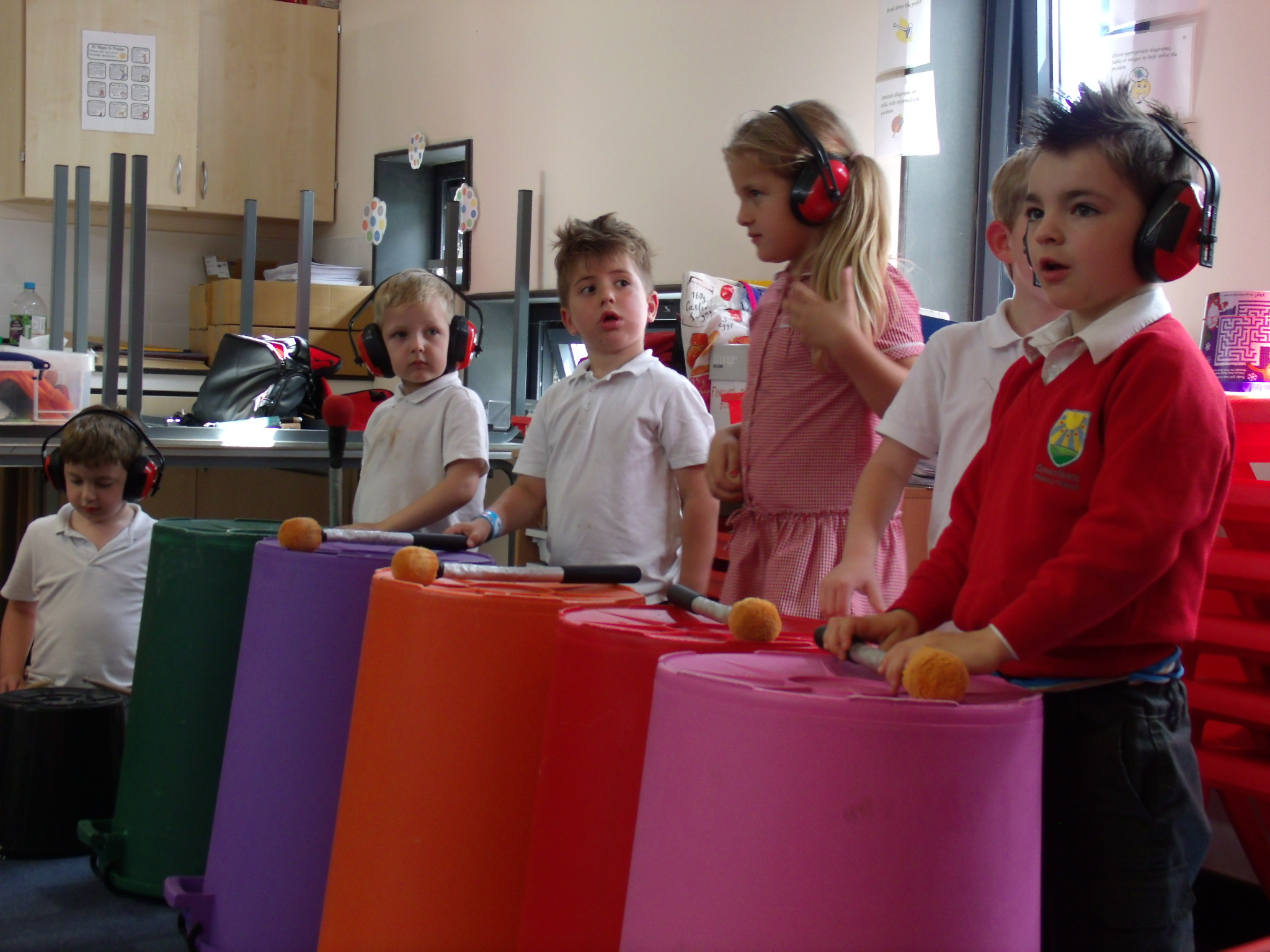 School children playing music on large colourful empty bins