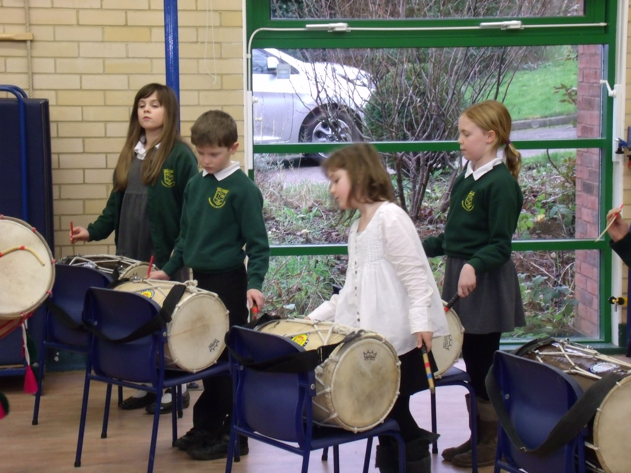 School children playing Indian drums in school hall on chairs